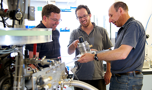 Three male researchers examining equipment in a cryostat laboratory